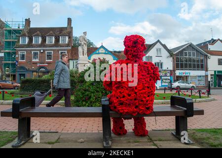 Chesham, Buckinghamshire. VEREINIGTES KÖNIGREICH. 11. November 2022. Eine auffällige Figur zum Gedenktag, in der ein Mann mit roten Mohnblumen auf einem Sitz in Chensham neben dem Kriegsdenkmal sitzt und eine weiße Taube in der Hand hält. Quelle: Maureen McLean/Alamy Live News Stockfoto