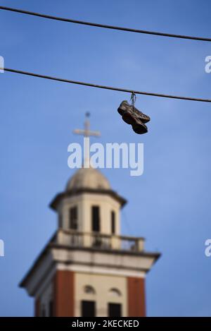 Paar Turnschuhe, die auf dem Kabel mit Glockenturm auf dem Hintergrund hängen Stockfoto