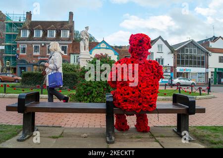 Chesham, Buckinghamshire. VEREINIGTES KÖNIGREICH. 11. November 2022. Eine auffällige Figur zum Gedenktag, in der ein Mann mit roten Mohnblumen auf einem Sitz in Chensham neben dem Kriegsdenkmal sitzt und eine weiße Taube in der Hand hält. Quelle: Maureen McLean/Alamy Live News Stockfoto