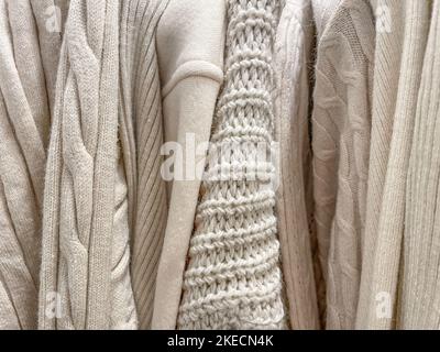 Textur Cosy Hintergrund Foto von verschiedenen gestrickten Pullover und Pullover in beige cremefarben hängen im Stapel in einem Geschäft. Herbst Winter warme Kleidung kol Stockfoto