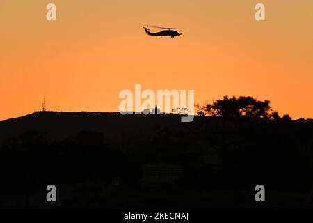 Der Hubschrauber MH-60 der US-Marine fliegt bei Sonnenuntergang in der Nähe des Cabrillo National Monument in San Diego, Kalifornien, von Coronado aus gesehen Stockfoto