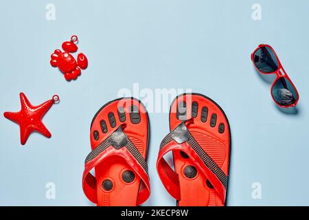 Zwei Paar Flip Flops auf blauem Hintergrund mit roten Schuhen und Seesternen im Vorderauge Stockfoto