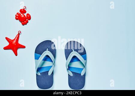 Zwei Paar blaue Flipflops und ein rotes Seesterne-Spielzeug auf weißem Hintergrund mit Platz für Text Stockfoto