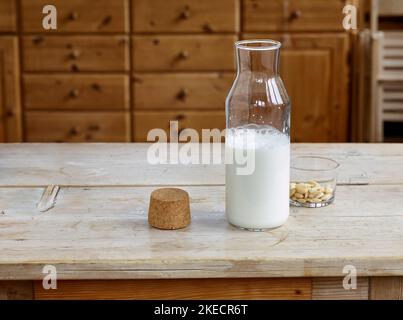 Schritte für die Herstellung von Mandelmilch, fertige Mandelmilch in einer Glasflasche mit Kork und einer Glasschale mit blanchierten Mandeln auf einem Holztisch Stockfoto