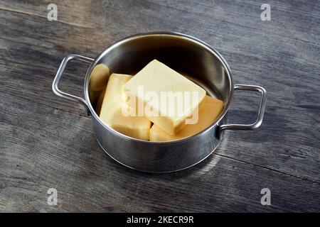 ayurvedische Ernährung, Schritte zur Zubereitung von hausgemachtem Ghee aus Butter - drei Stücke Bio-Sauerrahm-Butter in einem Edelstahl-Kochtopf auf einer dunklen Holzplatte Stockfoto