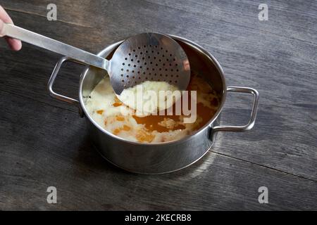 ayurvedische Ernährung, Schritte zur Zubereitung von hausgemachtem Ghee aus Butter - geschmolzene saure Rahmbutter in einem Edelstahltopan auf einer dunklen Holzplatte wird der Eiweißschaum mit einer Pfanne abgekocht Stockfoto