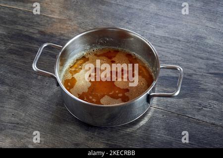 ayurvedische Ernährung, Schritte zur Zubereitung von hausgemachtem Ghee aus Butter - geschmolzene saure Rahmbutter in einem Edelstahltopan auf einer dunklen Holztischplatte, klärt das Ghee Stockfoto