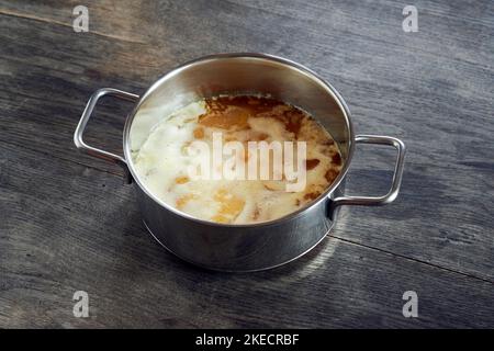 ayurvedische Ernährung, Schritte zur Zubereitung von hausgemachtem Ghee aus Butter - geschmolzene saure Rahmbutter in einem Edelstahltopan mit eiweißem Settling auf einer dunklen Holzplatte Stockfoto