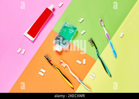 Zahnbürsten und Zahnpasen auf einer mehrfarbigen Oberfläche mit verschiedenen Farben, darunter Pink, Grün, Orange, Gelb Stockfoto