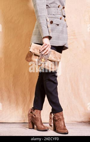 Eine Frau in einem Anzug und Stiefeln, die eine Handtasche hält, während sie mit dem rechten Bein nach oben zur Kamera geht Stockfoto