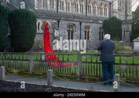 Beaconsfield, Buckinghamshire, Großbritannien. 11.. November 2022. Ein Mann hält an, um ein gestricktes Mohndenkmal am Gedenktag auf dem Gelände der Pfarrkirche St. Mary and All Saints in Beaconsfield, Buckinghamshire, zu fotografieren. Quelle: Maureen McLean/Alamy Live News Stockfoto