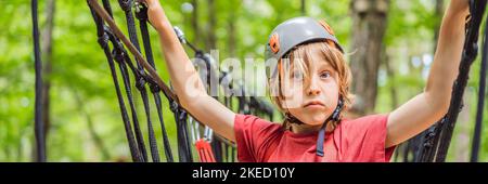 BANNER, LANG FORMAT glückliches Kind im Helm, gesunder Teenager Schuljunge, der an einem Sommertag in einem Kletterabenteuer-Park aktiv ist Porträt eines Stockfoto