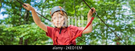 BANNER, LANG FORMAT glückliches Kind im Helm, gesunder Teenager Schuljunge, der an einem Sommertag in einem Kletterabenteuer-Park aktiv ist Porträt eines Stockfoto