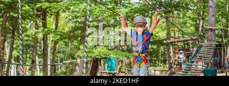 BANNER, LANG FORMAT glückliches Kind im Helm, gesunder Teenager Schuljunge, der an einem Sommertag in einem Kletterabenteuer-Park aktiv ist Porträt eines Stockfoto
