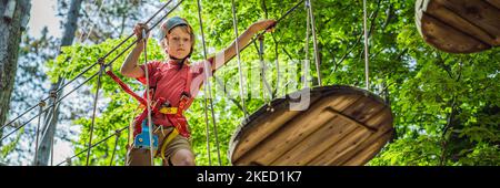 BANNER, LANG FORMAT glückliches Kind im Helm, gesunder Teenager Schuljunge, der an einem Sommertag in einem Kletterabenteuer-Park aktiv ist Porträt eines Stockfoto