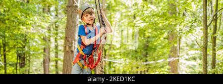 BANNER, LANG FORMAT glückliches Kind im Helm, gesunder Teenager Schuljunge, der an einem Sommertag in einem Kletterabenteuer-Park aktiv ist Porträt eines Stockfoto