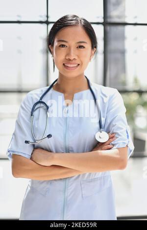Porträt einer asiatischen Ärztin, die mit gekreuzten Armen auf die Kamera schaut Stockfoto