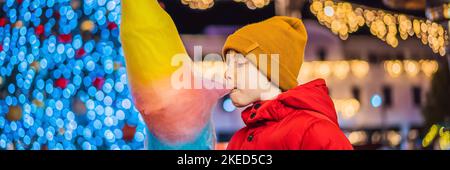 BANNER, LANGFORMATIGER Junge mit Zuckerwatte auf dem weihnachtsmarkt. Glückliches Kind auf dem Weihnachtsmarkt. Traditionelle Freizeitangebote für Familien an Weihnachten Stockfoto