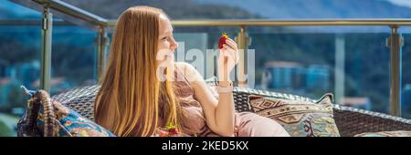 Portrait einer wunderschönen Frau in einem schönen Kleid auf einer Terrasse sitzen und essen Erdbeer-BANNER, LANG FORMAT Stockfoto