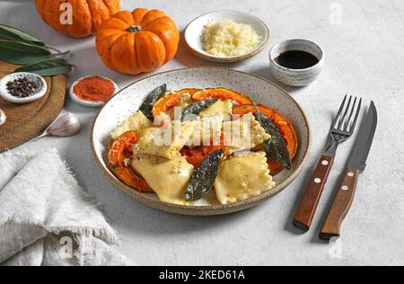 Hausgemachter Kürbis Ravioli mit Ricotta-Käse serviert Salbei und Hartkäse auf dem Teller auf einem Betontisch mit Gewürzen Stockfoto