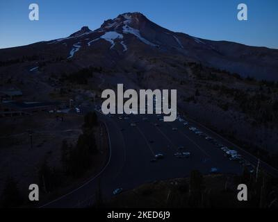 Hoher Berg, schneebedeckte Bergkette. Asphaltparkplatz am Fuße des Berges. Schöne Landschaft in der Dämmerung, Pinien. Reisen, Tourismus Stockfoto