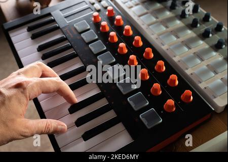 Nahaufnahme. MIDI-Keyboard und Musikerhand auf den Tasten. Minimalismus. Moderne Musikausrüstung, neue Technologien. Berufliche Tätigkeit eines Musikers, Stockfoto