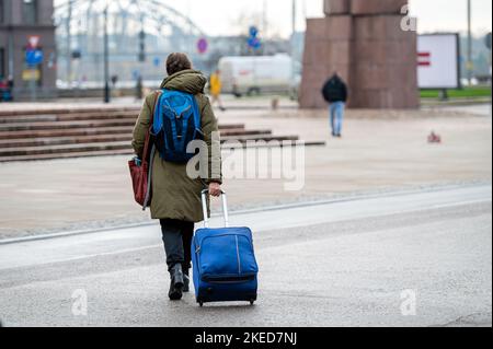 Ein Tourist mit Rucksack zieht einen Koffer auf Rädern die Straße hinunter, Rückansicht, Riga, Lettland Stockfoto