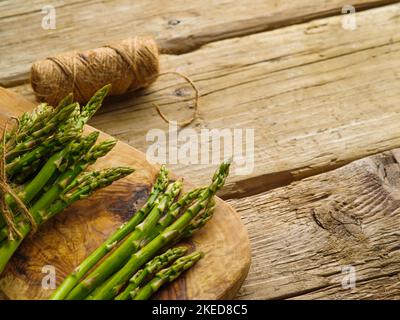 Nahaufnahme. Auf einem einfachen Holztisch befinden sich Spargelbüschen auf einem Schneidebrett und ein Garnklee. Nützliche vegetarische Produkt, Vitamine, Antioxidantien. Stockfoto