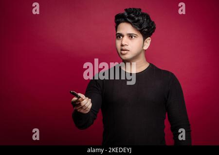 Ein wütender, emotionaler junger Mann, der isoliert über einem roten Wandhintergrund steht Stockfoto
