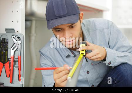 Junger Handwerker, der PVC-Rohr misst Stockfoto