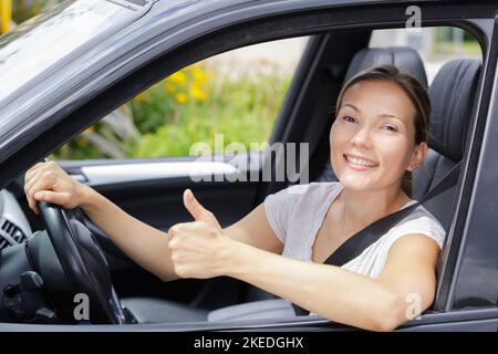 Junge Fahrerin hinter dem Steuer, die Daumen nach oben Geste macht Stockfoto