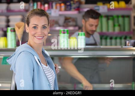 Glückliche junge Frau, die sich aus einem Glasschrank im Lebensmittelgeschäft auswählt Stockfoto