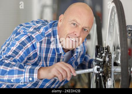 Lächelnder Mechaniker mit männlichem Lächeln überprüft die Reifen auf einem Fahrrad Stockfoto