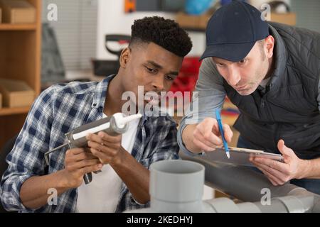 Junger Arbeiter, der etwas über Kunststoffrohre lernt Stockfoto