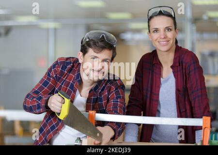 Ein glücklicher Mann verwendet eine Handsäge mit einem Kollegen Stockfoto