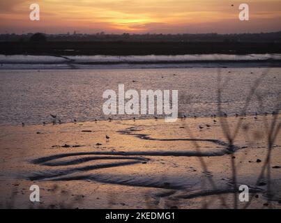 Sonnenuntergang über dem Fluss Adur bei Ebbe mit Start- und Landebahn des Flughafens Brighton City und Lancing im Hintergrund. Stockfoto