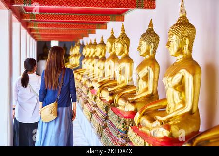 Asiatische Touristen gehen im Foyer einer Reihe von Buddha-Statuen Wat Phra Chetuphon (Wat Pho), Bangkok, Thailand. Stockfoto