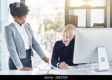 Sie sind nie zu alt, um von Ihren Mitarbeitern zu lernen. Eine junge Geschäftsfrau zeigt ihrem Kollegen etwas auf einem Tablet. Stockfoto