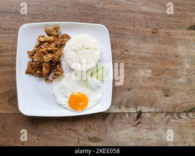 Moo tod oder Gratiem. Frittiertes Schweinefleisch mit Knoblauch und Pfeffer auf einem weißen Teller mit Holzhintergrund. Thai Street Food in Thailand. Stockfoto