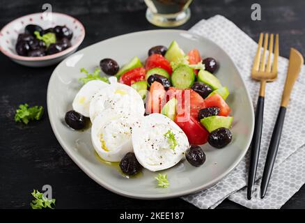 Griechischer Salat aus frischer Gurke, Tomaten, Burrata-Käse und schwarzen Oliven mit Olivenöl. Gesunde Ernährung. Stockfoto