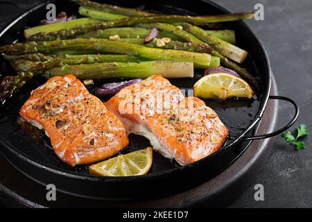 Köstlicher gebackener Lachs mit Spargel, Zitronenscheiben und Gewürzen auf dunklem Tisch. Stockfoto