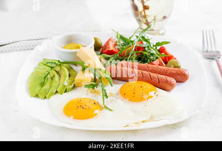 Englisches Frühstück - Spiegeleier, Würstchen, Tomaten, Avocado, Käse und Oliven. Amerikanisches Essen. Stockfoto