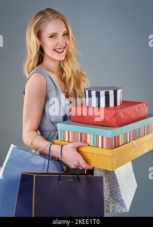 Er leistet einen großen Beitrag zur wirtschaftlichen Gesundheit. Beschnittene Studioaufnahme einer glücklichen jungen Frau mit einer Auswahl an Einkaufstaschen und Geschenkboxen. Stockfoto