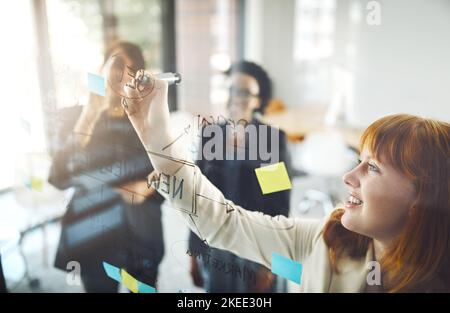 Teilen ihre Ideen mit dem Team. Drei Geschäftsfrau mit einem Glaswischbrett während einer Brainstorming-Sitzung. Stockfoto