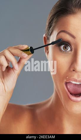 Meine Wimpern lieben diese neue Mascara. Studioportrait einer schönen jungen Frau, die vor grauem Hintergrund Mascara aufsetzt. Stockfoto