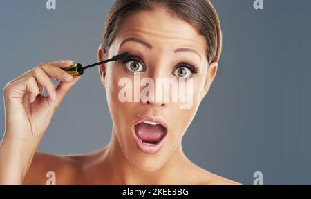 Sie pumpt ihre Wimpern hoch. Studioportrait einer schönen jungen Frau, die vor grauem Hintergrund Mascara aufsetzt. Stockfoto