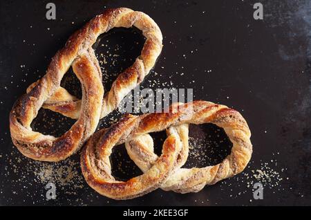 Frisch gebackene Brezeln mit Zucker auf altem schwarzen Metallhintergrund, Nahaufnahme, Draufsicht Stockfoto