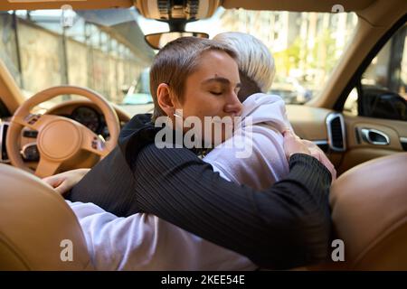 Brunette umarmt eine Blondine im Inneren des stilvollen Autos Stockfoto