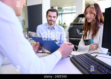 Auto-Verkaufsberater zeigt Fahrzeugkäufern die Dokumentation Stockfoto
