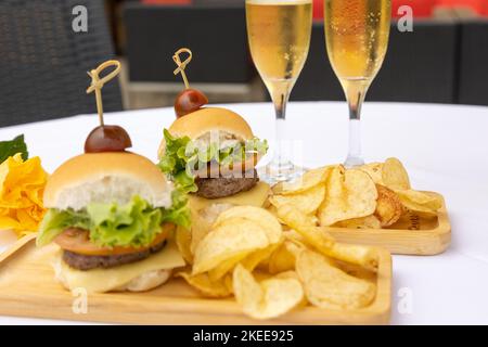 Eine obere Nahaufnahme von Burger und Chips auf den Holztellern, zwei Gläser voller Champagner, weißer Hintergrund Stockfoto